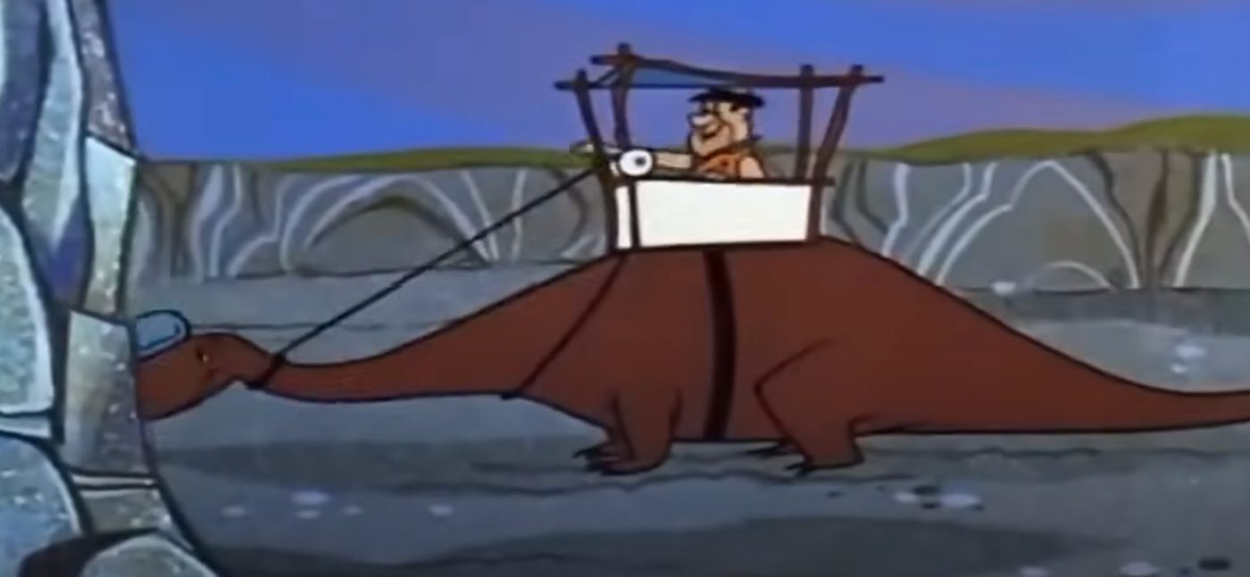 Fred Flintstone operating a stone-age excavator — a humorous nod to the eternal operator